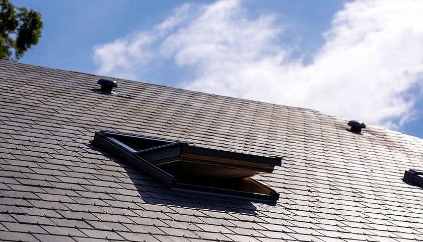 A view of a roof on a sunny day with an open attic window.